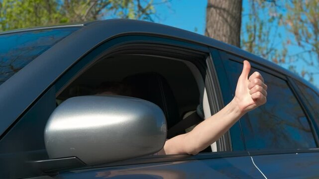 Female driver show thumb up. A view of joyful female show the thumb up from the auto cabin. A concept of happy driving tour.