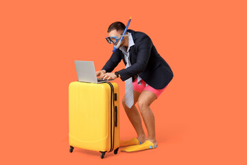 Young office worker in diving mask with laptop and suitcase on orange background