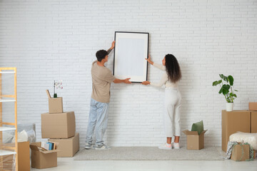 Young happy couple hanging picture frame near cardboard boxes in their new flat