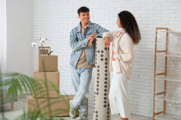 Fototapeta premium Young happy couple with carpet near cardboard boxes in their new flat