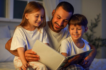 Obraz premium Father and his little children reading book at night
