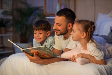 Father and his children reading book on bed in room