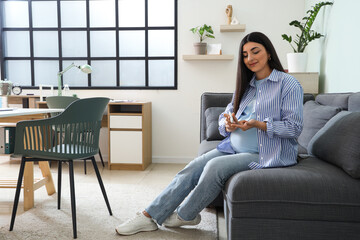 Young pregnant woman with gestational diabetes using lancet pen on sofa in clinic