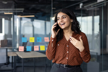 A cheerful businesswoman is engaged in a lively phone conversation in a contemporary office...