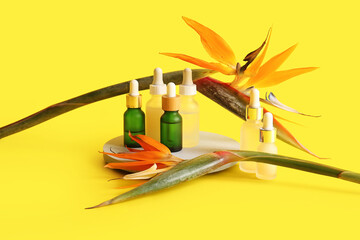 Bottles of cosmetic products and beautiful strelitzia flowers on yellow background