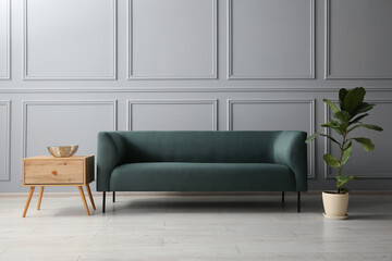 Stylish sofa, bowl on side table and green plant near grey wall