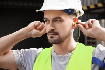 Male builder putting in earplugs outdoors, closeup