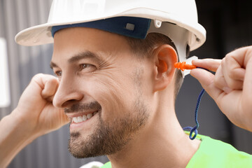 Male builder putting in earplugs outdoors, closeup