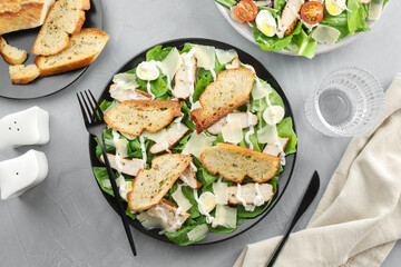 Delicious Caesar salad with chicken served on grey textured table, flat lay