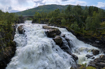 Powerful waterfall cascading over rugged rocks, surrounded by lush greenery.