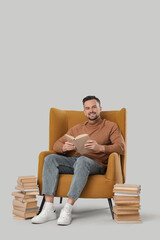 Handsome man reading book in armchair on light background