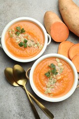 Delicious sweet potato soup with pumpkin seeds in bowls and fresh vegetables on grey textured table, flat lay