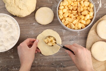 Woman making pirozhki (stuffed pastry pies) with apples at wooden table, top view