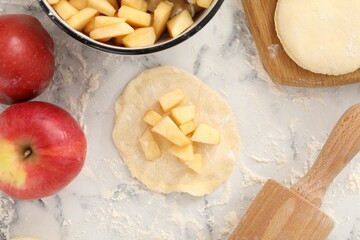 Making pirozhki (stuffed pastry pies). Pieces of dough with apples on white marble table, flat lay