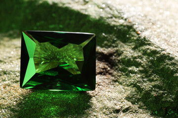 Beautiful shiny green gemstone on stone, closeup. Space for text