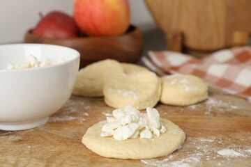 Making pirozhki (stuffed pastry pies). Pieces of dough with cottage cheese on wooden table, closeup