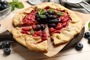 Tasty galette with strawberries, blueberries and mint on wooden table, closeup