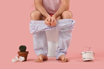 Suffering man with cactus, paper and barbed wire sitting on toilet bowl against pink background....