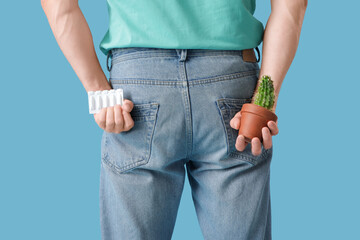 Man with cactus and suppositories on blue background, closeup. Hemorrhoid concept