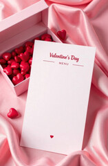 Valentine&rsquo;s Day menu mockup featuring a blank card on pink silk fabric with a box of red heart-shaped chocolates, perfect for romantic and festive designs