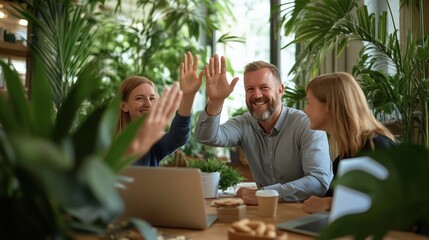 Fototapeta premium Business team high-fiving at a table in a green office environment, collaboration
