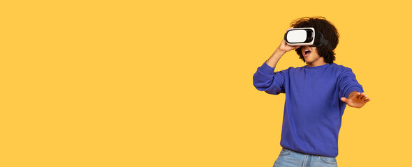 A young black man interacts with virtual reality gear, showcasing excitement in a bright, isolated studio. His casual attire reflects a hipster lifestyle while exploring new digital worlds, copy space