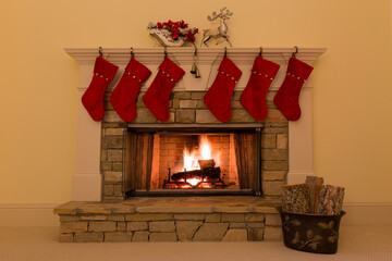 Six red Christmas stockings adorn a stone fireplace with a cozy fire.
