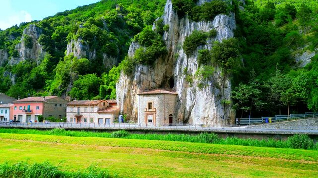 Charming aerial pedestal up shot from Pioraco, a vision of the Eremo della Madonna della grotta coming out of the Sibillini mountains, their rocky surfaces covered by greenery, road, buildings, meadow