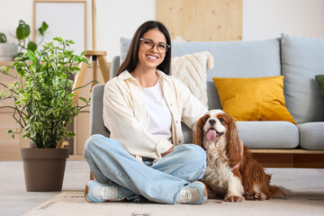 Beautiful young woman with cute cavalier King Charles spaniel sitting on floor at home