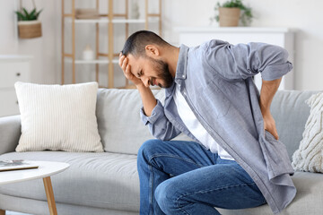 Fototapeta premium Young man suffering from back pain on sofa at home