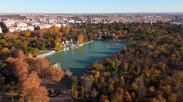 Incredibly stunning and cinematic aerial view of El Retiro Park in Madrid, showcasing the vibrant hues of autumn and a tranquil lake nestled in the heart of the bustling city, perfect for relaxation