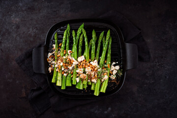 Green asparagus glazed with Greek feta cheese, roasted pine nuts and cress on served as top view in...