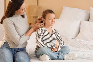 Mother putting hearing aid in her little daughter's ear at home