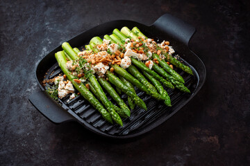 Green asparagus glazed with Greek feta cheese, roasted pine nuts and cress on served as close-up in...