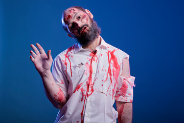 Portrait of man dressed as sinister zombie covered in blood for halloween event waving hand towards...