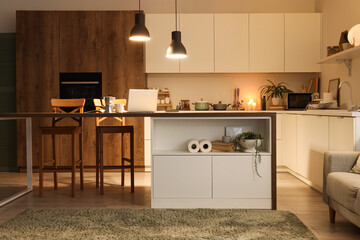 Interior of kitchen with table, counters and glowing lamps in evening