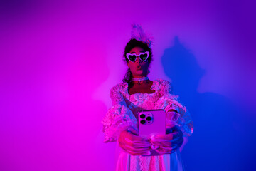 Elegant young woman in heart-shaped sunglasses takes a selfie against vibrant pink and violet lighting