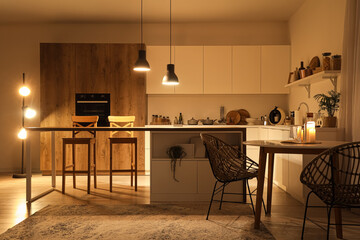 Interior of modern kitchen with tables, counters and glowing lamps in evening
