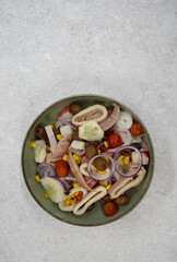 Seafood salad. Top view of a mediterranean salad with squid, onion, cherry tomatoes, corn grains, cucumber and black olives, in a bowl with a white background