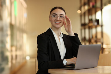 Woman in stylish formal suit working on laptop at table indoors