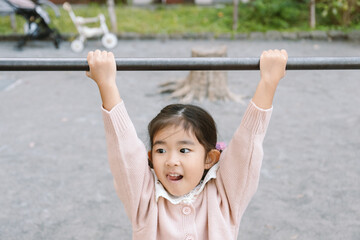 Fototapeta premium Cute asian girl hanging from a horizontal bar at the playground in Tokyo Japan