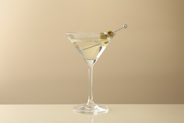 Martini cocktail with olives in glass on beige table