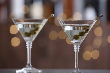 Martini cocktail with olives in glasses on wooden table against blurred background, closeup. Bokeh effect