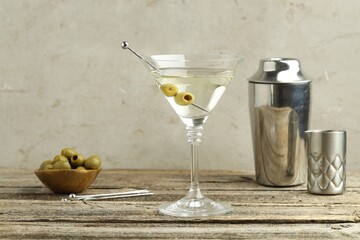 Martini cocktail with olives in glass and shaker on wooden table