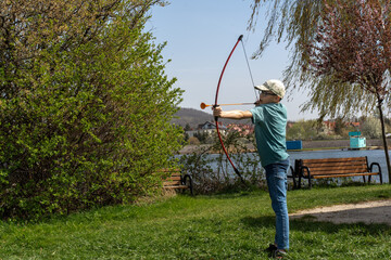 Young boy practicing archery with a toy bow and arrow in a park on a sunny day. Concept of outdoor...