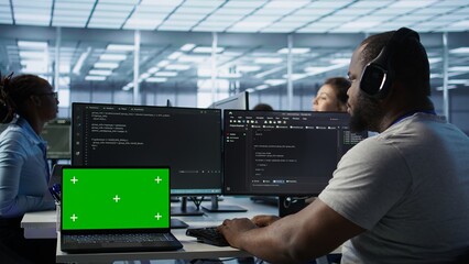 Isolated screen laptop next to programmer coding in server farm while listening music in...