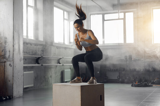 A fit woman is energetically performing a dynamic box jump in a modern gym, showcasing her strength and agility