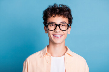 Happy young man with glasses and braces wearing a trendy shirt against a blue background