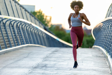 Female black athlete stride running outdoors in Boston bridge