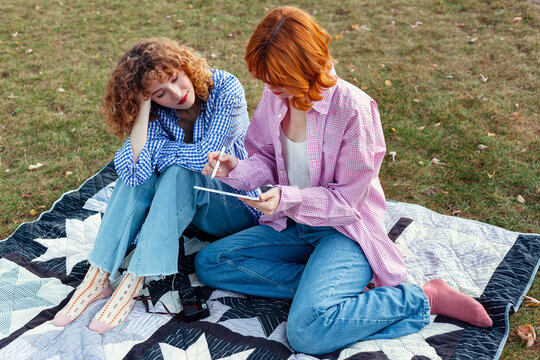 Friends enjoying creative afternoon outdoors while sketching on tablet